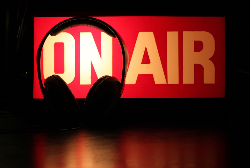 Headphones silhouette against On-Air sign symbolising a podcast broadcast.